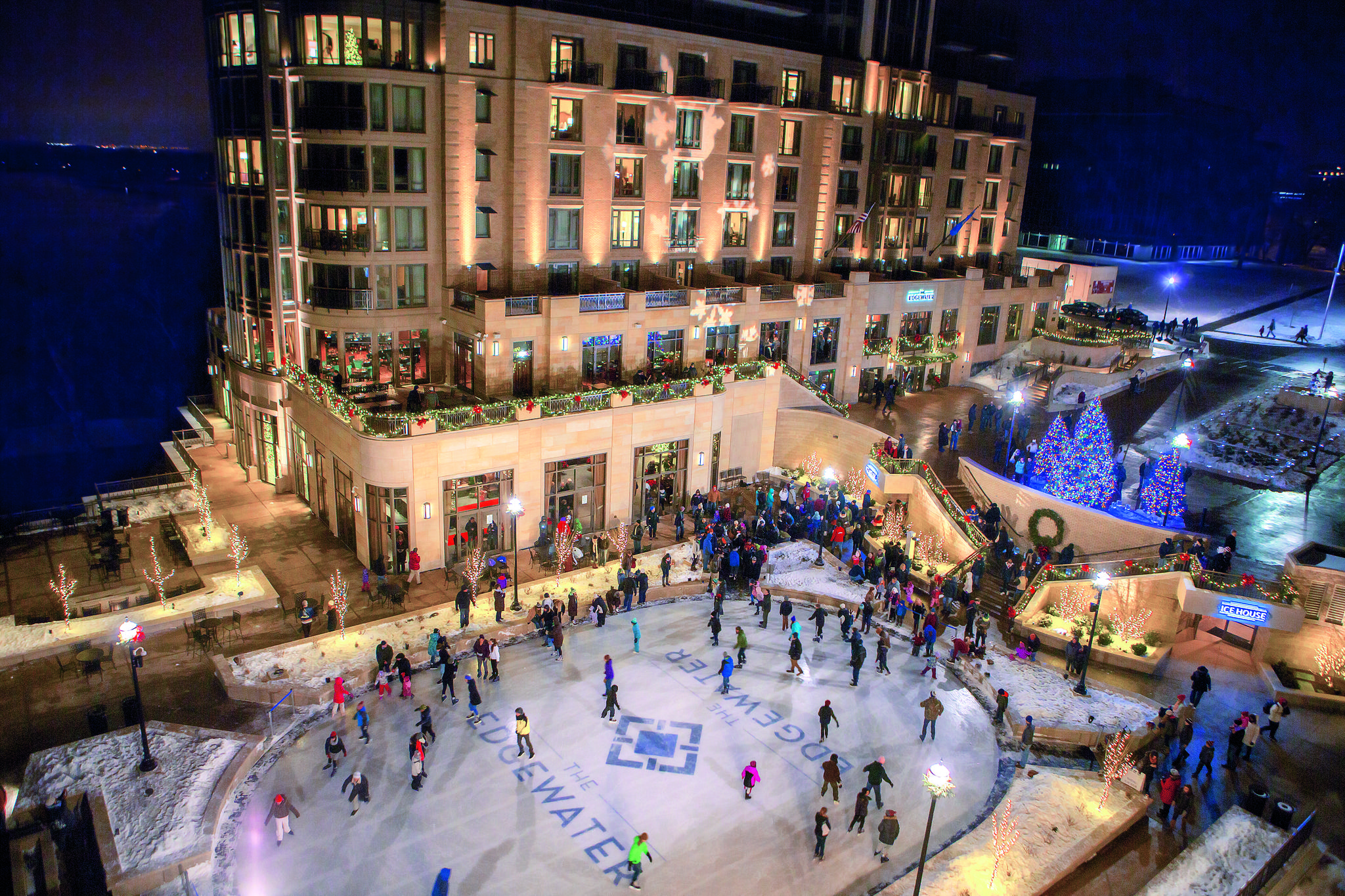 Skaters enjoy a festive outdoor ice rink surrounded by holiday lights and a beautifully decorated building at night.